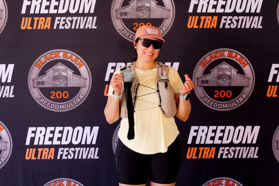 Smiling runner holding a finisher award in front of the Freedom Ultra Festival backdrop