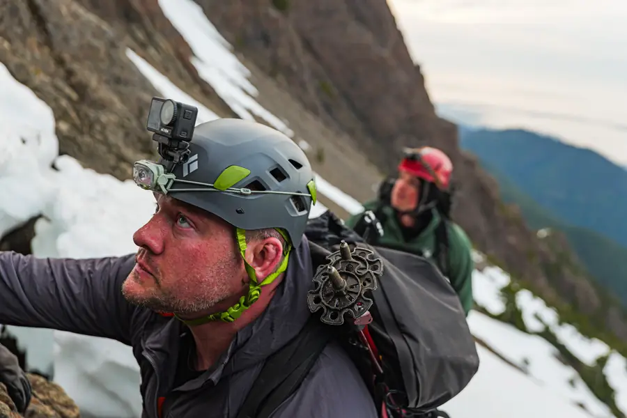 Climber in a helmet with an action camera looking up a snowy couloir
