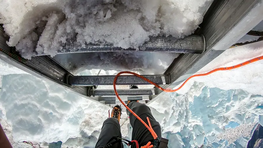 Point-of-view shot of mountaineering boots on a ladder crossing a glacier crevasse