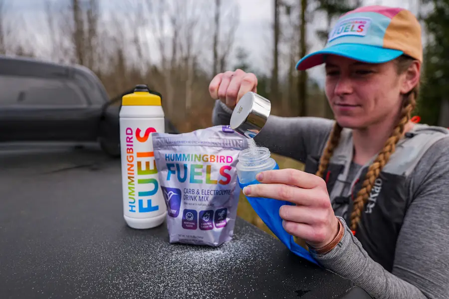 Trail runner pouring Hummingbird Fuels drink mix into a soft flask at the trailhead