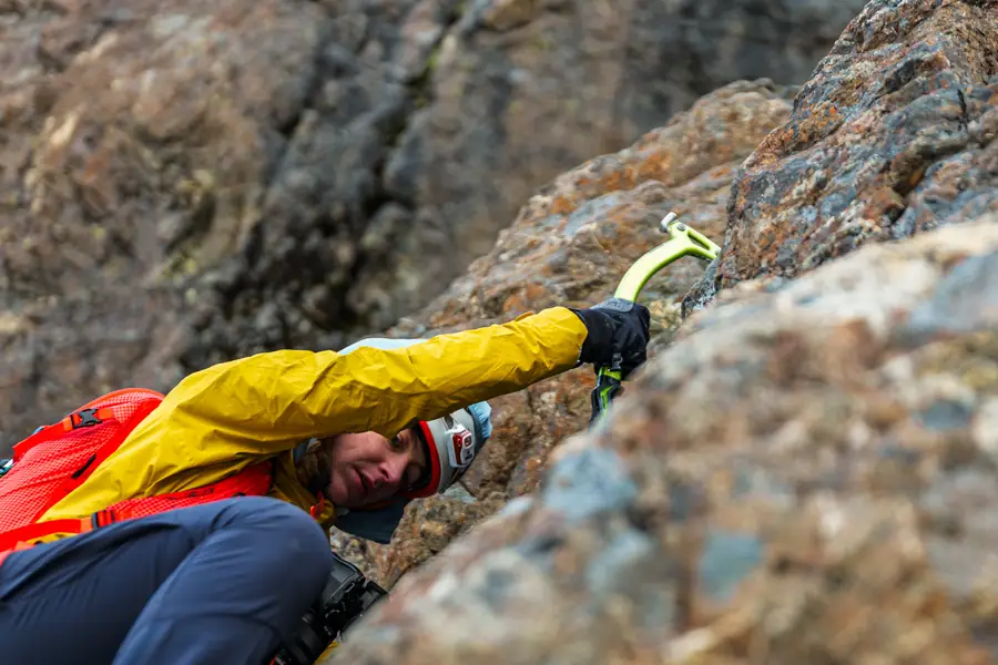 Climber placing an ice axe while scrambling up a rock face