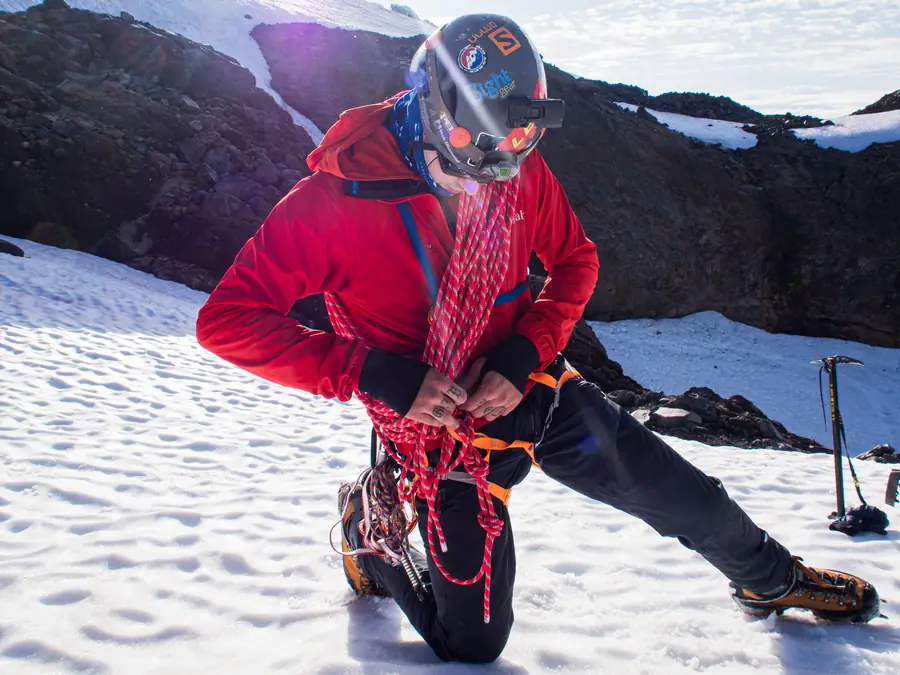 Mountaineer kneeling in snow coiling a red climbing rope