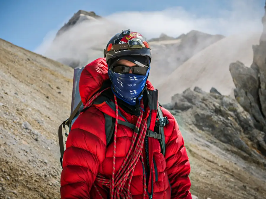 Mountaineer in a red down jacket carrying a rope on an alpine ridge