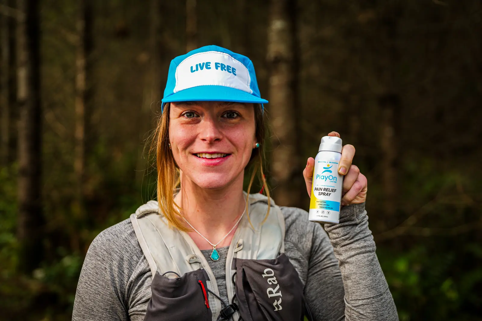 Trail athlete in a running vest holding a recovery spray product in a forest, outdoor product photography by Ultra Nomadic Media