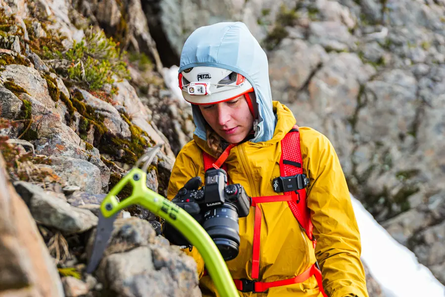 Photographer in a yellow jacket climbing rock with a camera and ice axe