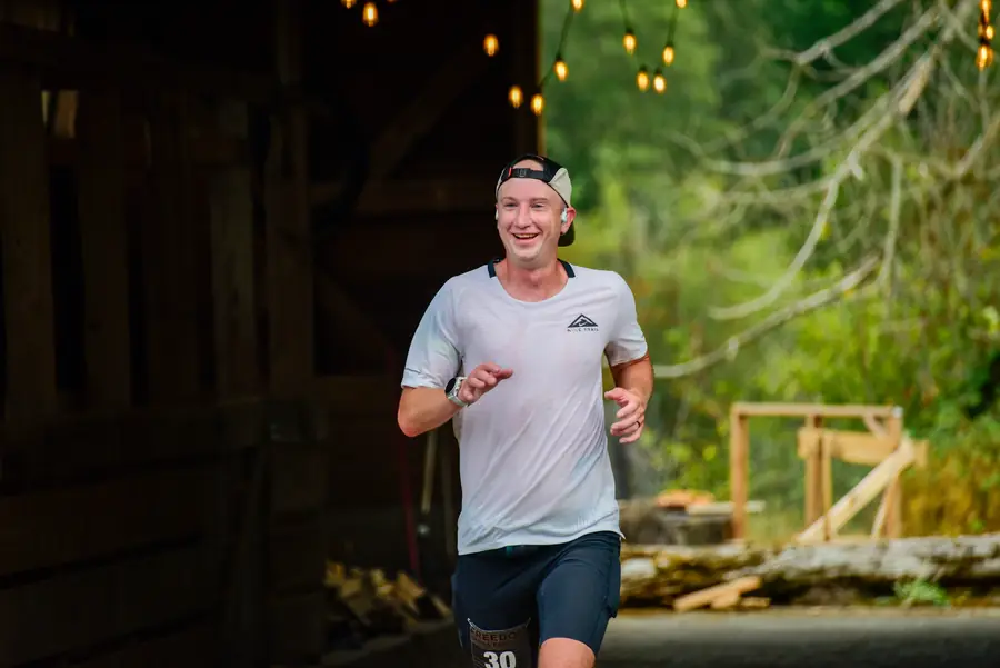 Ultra runner smiling as he runs out of a string-lit barn aid station