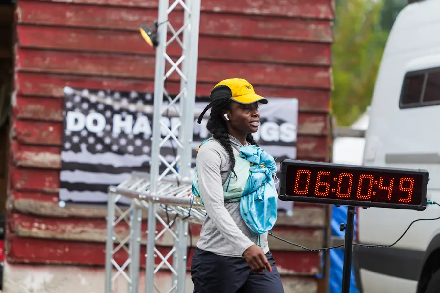 Ultra runner passing the race clock next to a red barn